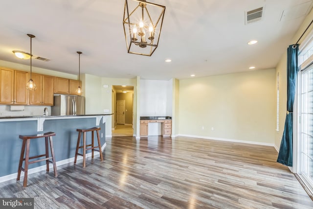 kitchen featuring light hardwood / wood-style flooring, a kitchen breakfast bar, hanging light fixtures, a chandelier, and stainless steel fridge