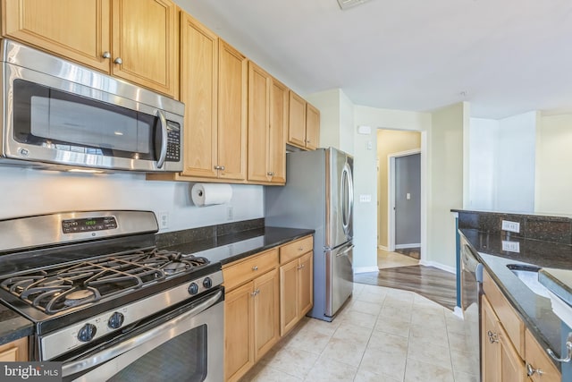 kitchen with light hardwood / wood-style floors, dark stone counters, and appliances with stainless steel finishes