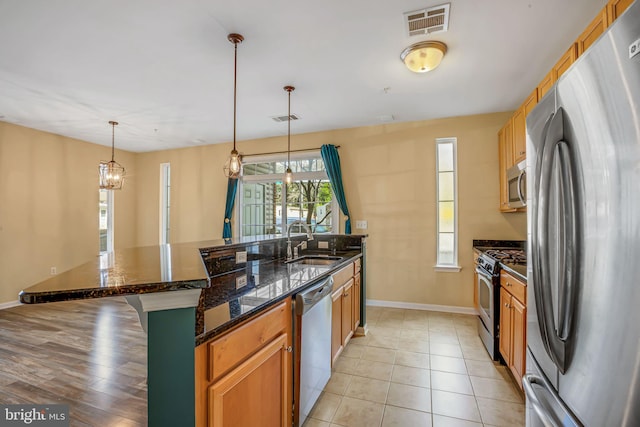 kitchen featuring stainless steel appliances, sink, decorative light fixtures, light hardwood / wood-style floors, and an island with sink