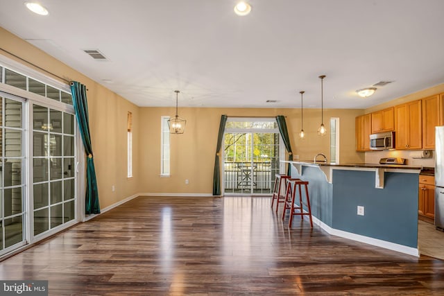 kitchen with sink, dark wood-type flooring, hanging light fixtures, stainless steel appliances, and a kitchen bar