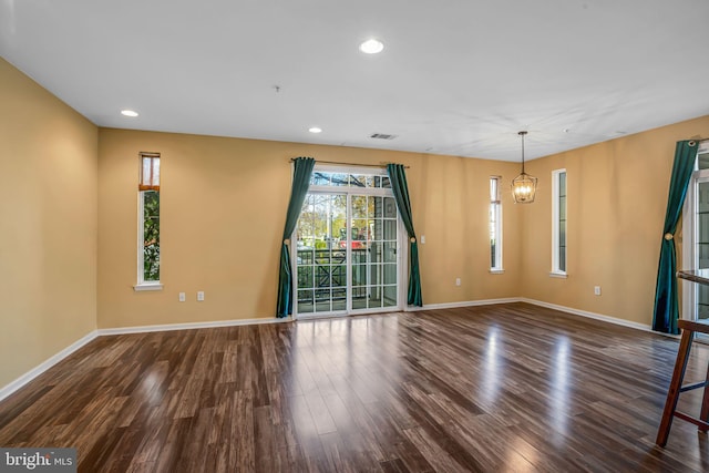 empty room with dark hardwood / wood-style flooring and a notable chandelier