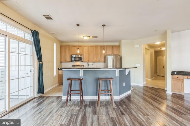 kitchen featuring a breakfast bar area, dark wood-type flooring, an island with sink, and stainless steel appliances