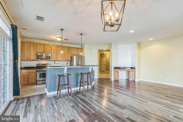 kitchen with a kitchen bar, appliances with stainless steel finishes, light wood-type flooring, pendant lighting, and a kitchen island