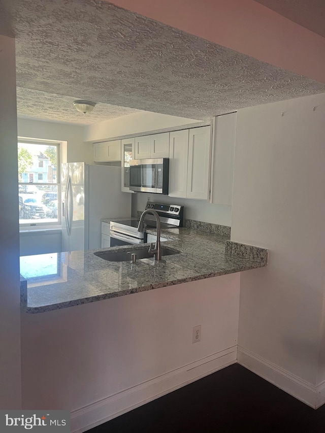 kitchen featuring white cabinetry, kitchen peninsula, appliances with stainless steel finishes, a textured ceiling, and stone counters