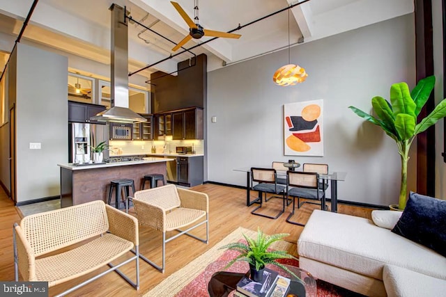 living room featuring a towering ceiling, light hardwood / wood-style floors, beamed ceiling, and ceiling fan