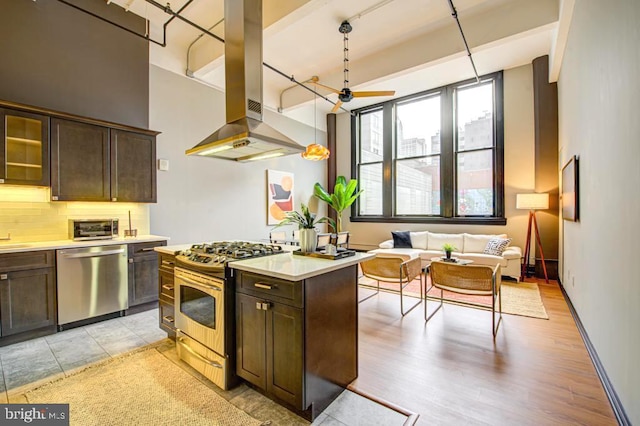 kitchen featuring stainless steel appliances, hanging light fixtures, island exhaust hood, dark brown cabinets, and light wood-type flooring