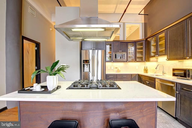 kitchen with island range hood, a kitchen island, appliances with stainless steel finishes, sink, and a breakfast bar area