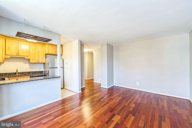 kitchen with light hardwood / wood-style flooring, sink, dark stone counters, and stainless steel fridge