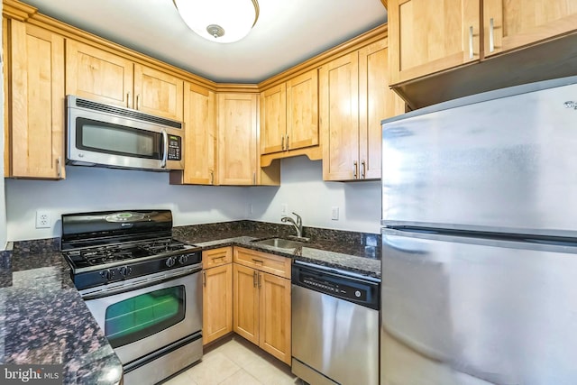 kitchen with dark stone countertops, appliances with stainless steel finishes, sink, and light tile patterned floors