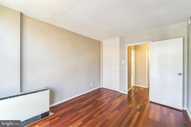 unfurnished bedroom with dark wood-type flooring, radiator heating unit, and a closet