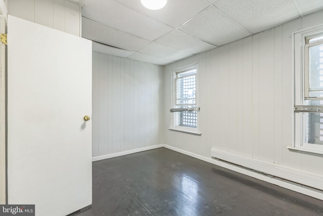 empty room featuring wood walls, a paneled ceiling, and a baseboard heating unit