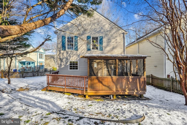 snow covered back of property featuring a deck and a sunroom