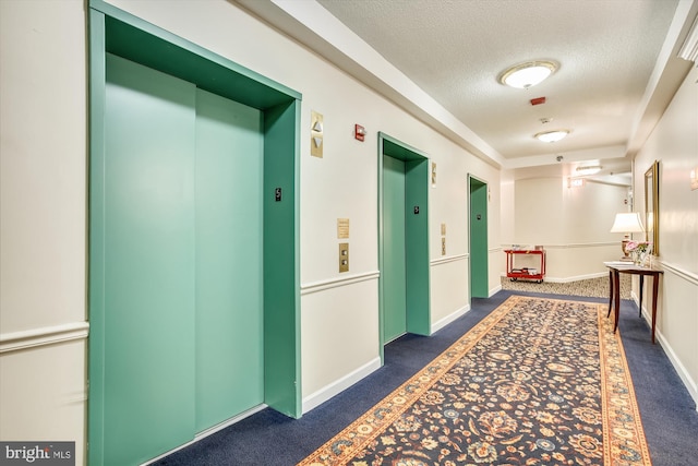 hallway with elevator, a textured ceiling, and dark colored carpet