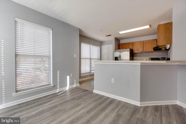 kitchen with stainless steel fridge with ice dispenser, light hardwood / wood-style flooring, and kitchen peninsula