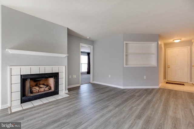 unfurnished living room with a fireplace, built in features, and light wood-type flooring