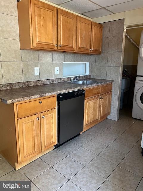 kitchen featuring stainless steel dishwasher, stacked washer and dryer, light tile patterned floors, and a paneled ceiling