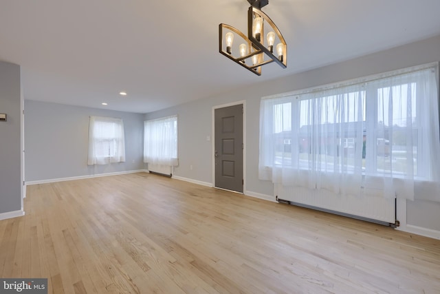 interior space featuring light hardwood / wood-style floors, a baseboard radiator, plenty of natural light, and a notable chandelier