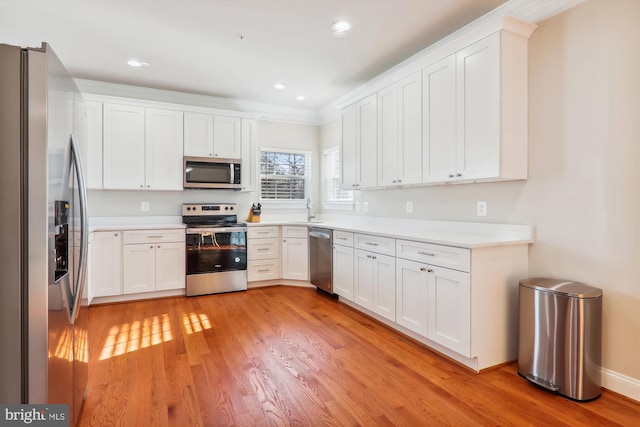 kitchen with appliances with stainless steel finishes, ornamental molding, sink, white cabinets, and light hardwood / wood-style floors