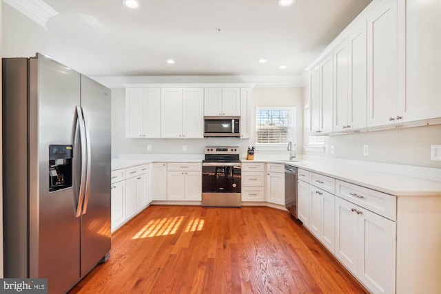 kitchen with sink, crown molding, light hardwood / wood-style floors, white cabinets, and appliances with stainless steel finishes