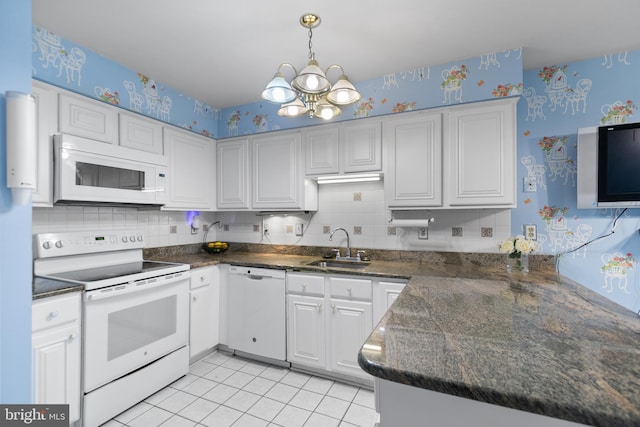 kitchen with white appliances, wallpapered walls, a chandelier, a sink, and white cabinets