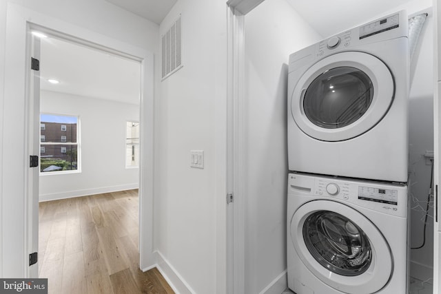 laundry room with light hardwood / wood-style floors and stacked washer / dryer