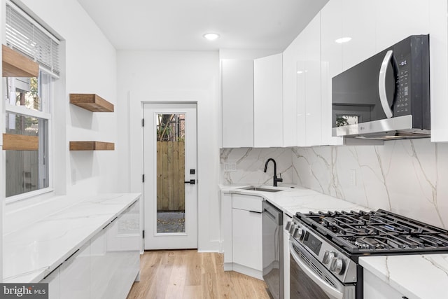 kitchen featuring stainless steel appliances, white cabinetry, sink, light stone counters, and light hardwood / wood-style flooring