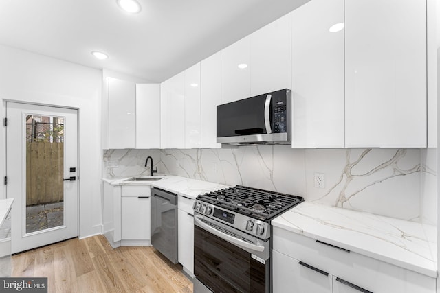 kitchen featuring white cabinetry, light wood-type flooring, appliances with stainless steel finishes, light stone countertops, and sink