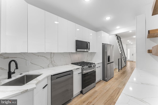 kitchen featuring light stone counters, white cabinets, light hardwood / wood-style flooring, sink, and appliances with stainless steel finishes