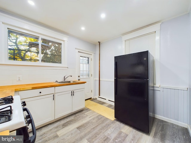 kitchen with gas range gas stove, sink, white cabinets, black refrigerator, and butcher block countertops