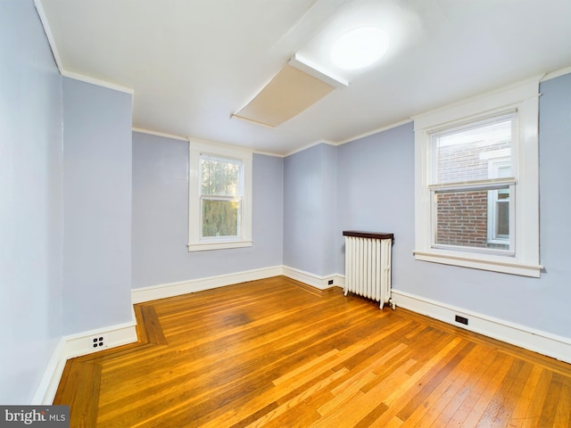 unfurnished room featuring radiator heating unit, hardwood / wood-style floors, and ornamental molding