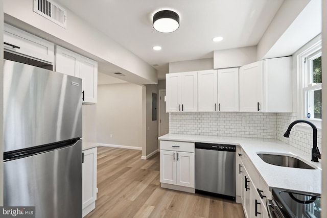 kitchen with light wood-type flooring, appliances with stainless steel finishes, sink, and white cabinets