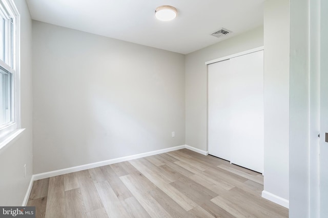 unfurnished bedroom with light hardwood / wood-style floors, multiple windows, and a closet