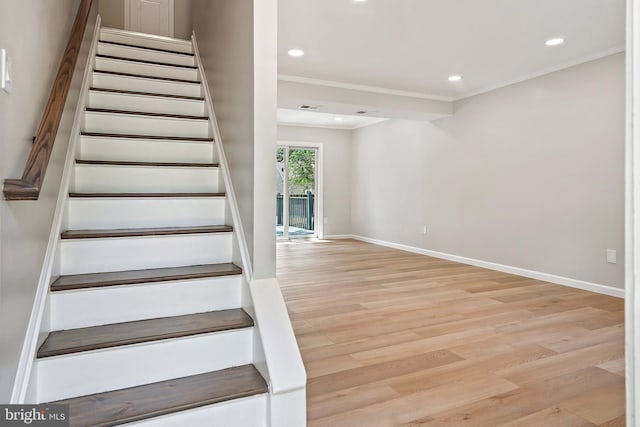 stairway with wood-type flooring and crown molding