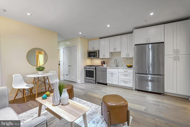 kitchen featuring sink, light hardwood / wood-style flooring, decorative backsplash, white cabinets, and appliances with stainless steel finishes