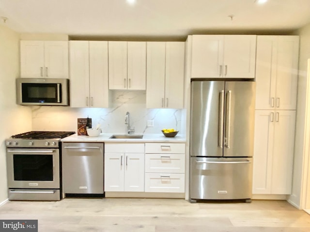 kitchen with appliances with stainless steel finishes, tasteful backsplash, sink, light hardwood / wood-style flooring, and white cabinets