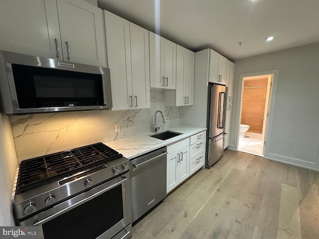 kitchen with sink, stainless steel appliances, white cabinetry, and light hardwood / wood-style flooring