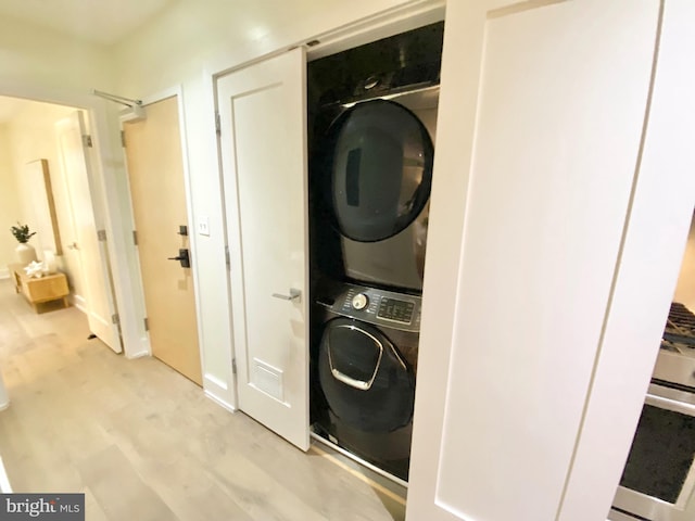 clothes washing area featuring stacked washer and dryer and light hardwood / wood-style flooring