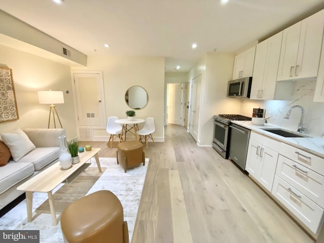 kitchen featuring white cabinetry, sink, light hardwood / wood-style floors, and appliances with stainless steel finishes