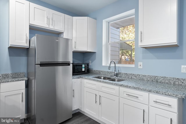 kitchen featuring white cabinetry, sink, light stone countertops, dark hardwood / wood-style floors, and stainless steel fridge