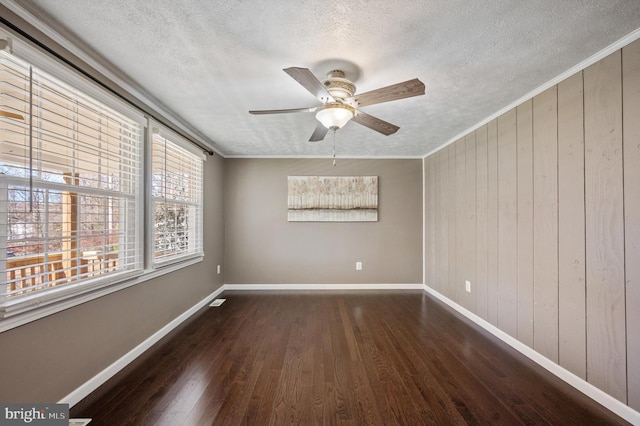 empty room featuring ceiling fan, dark hardwood / wood-style flooring, crown molding, a textured ceiling, and wooden walls