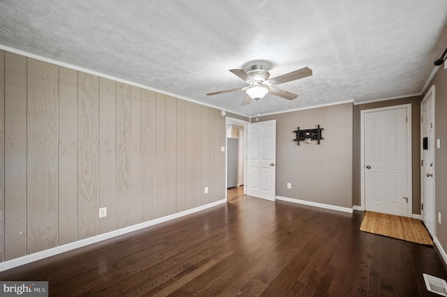 unfurnished room with crown molding, wooden walls, ceiling fan, a textured ceiling, and dark hardwood / wood-style flooring