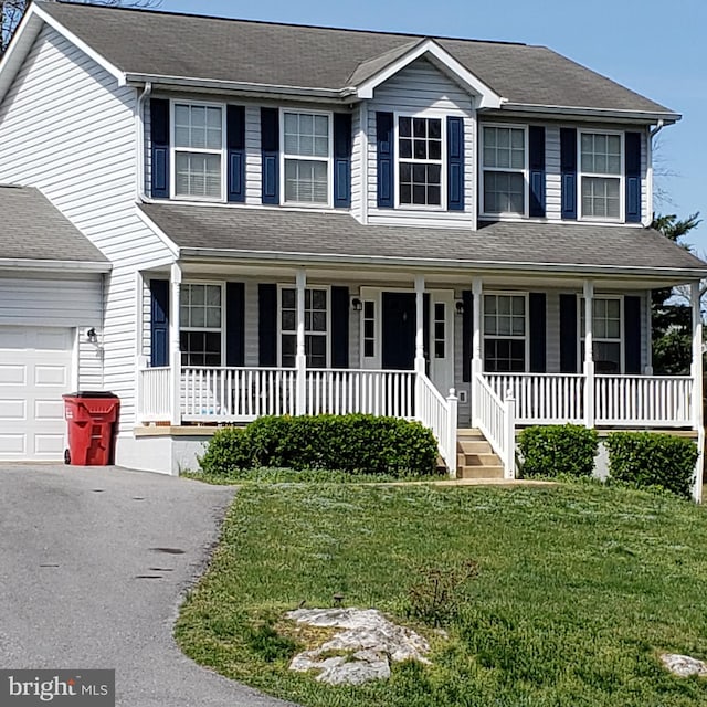 view of front of property featuring covered porch, a garage, and a front lawn