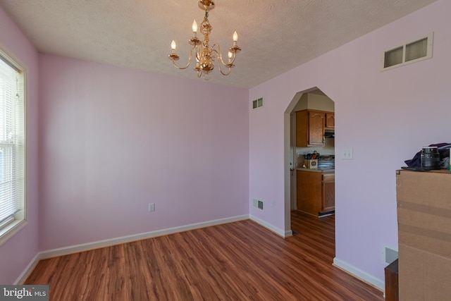 unfurnished dining area featuring a chandelier, a textured ceiling, and dark wood-type flooring