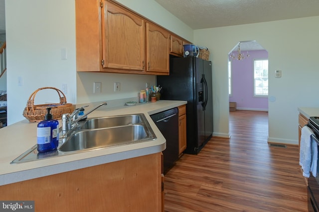 kitchen with dark wood-type flooring, black appliances, sink, a textured ceiling, and a notable chandelier