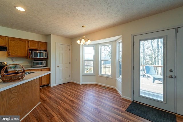 kitchen featuring pendant lighting, stainless steel microwave, sink, dark hardwood / wood-style flooring, and a chandelier