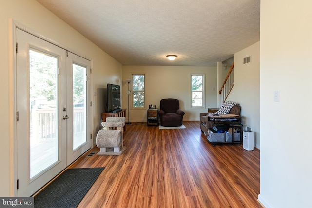 living area featuring a textured ceiling, plenty of natural light, dark wood-type flooring, and french doors