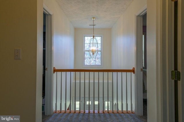 hallway with carpet, a textured ceiling, and a chandelier