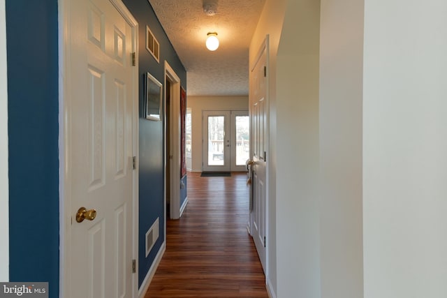 hallway with dark hardwood / wood-style floors, a textured ceiling, and french doors