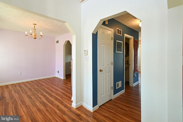 hallway featuring a textured ceiling, dark hardwood / wood-style flooring, and a notable chandelier