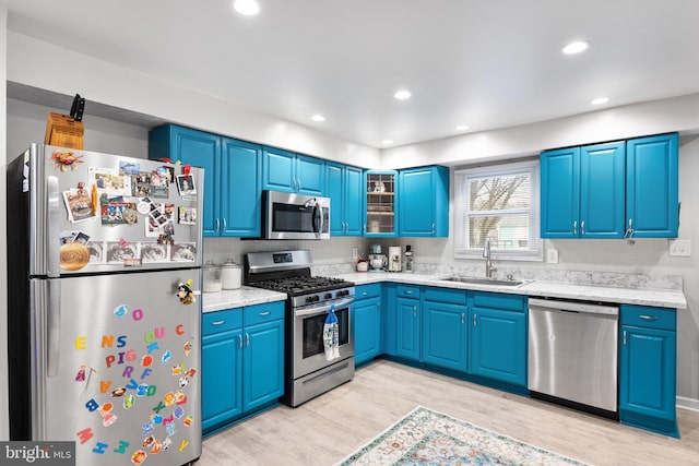 kitchen with blue cabinetry, appliances with stainless steel finishes, light wood-type flooring, and sink